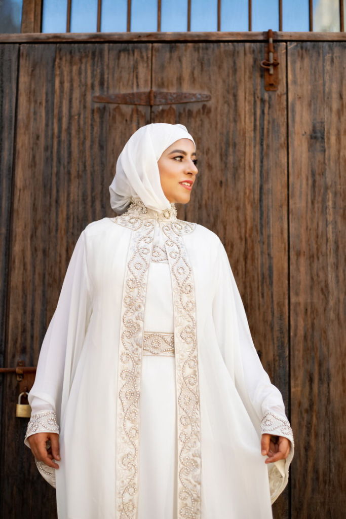 Lady wearing a white abaya with embroidered hems in curly lines.