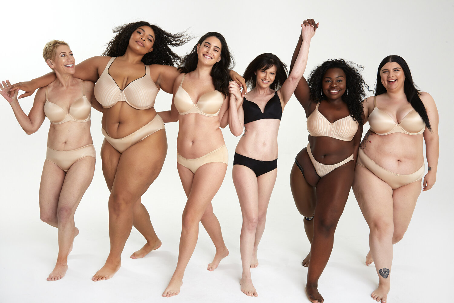 The image on a white background shows 6 very different women hugging and walking smiling towards the camera. Women of different height, age, body type, color, ability. All women are wearing different type of lingerie combos perfectly fitting.