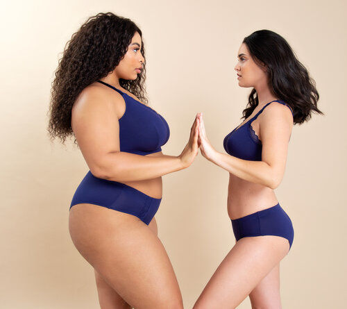 The image shows two women facing each other touching each other with their hands raised to the height of the torso. They have different stature and body type and wear the same lingerie pieces perfectly fitting both.