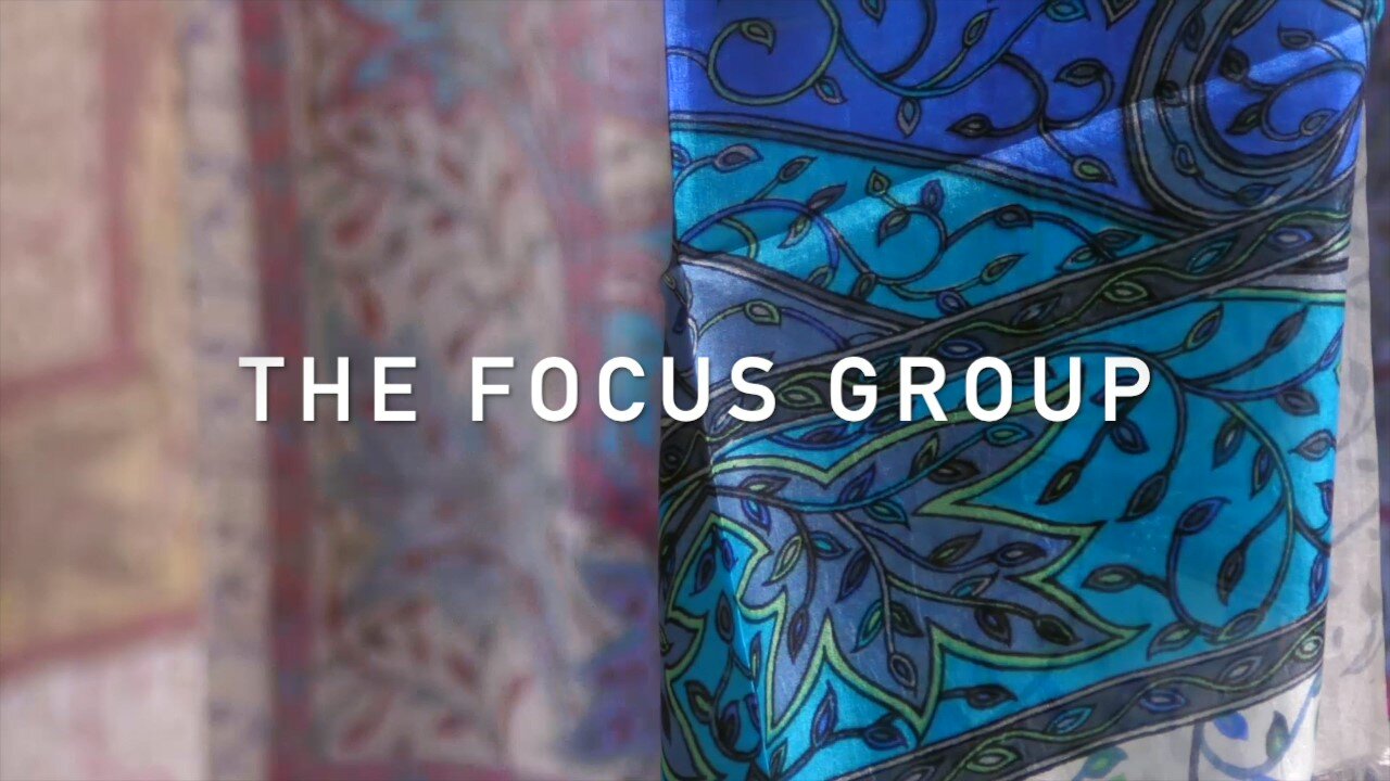 Image shows detail of a colorful silk shawl in shades of blue and green. Writing in white THE FOCUS GROUP