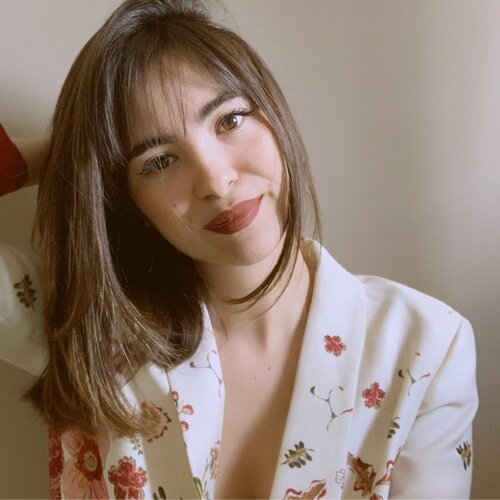 Picture of Alessia Migliaccio, contributor, young brunette lady with medium long hair. Alessia is wearing a white floral blouse and is smiling.